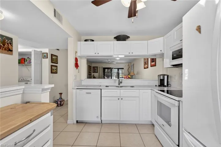 Kitchen featuring white cabinetry, light-toned countertops, a stainless steel sink, and white appliances including a refrigerator, dishwasher, and range