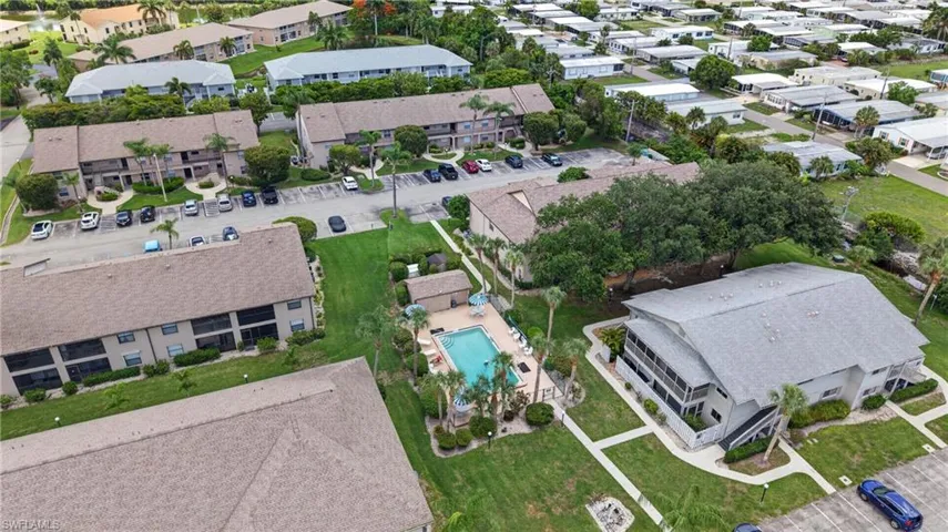 Aerial perspective showcasing a residential community with multiple multi-story buildings, a central swimming pool with lounge area, manicured green spaces, and ample parking