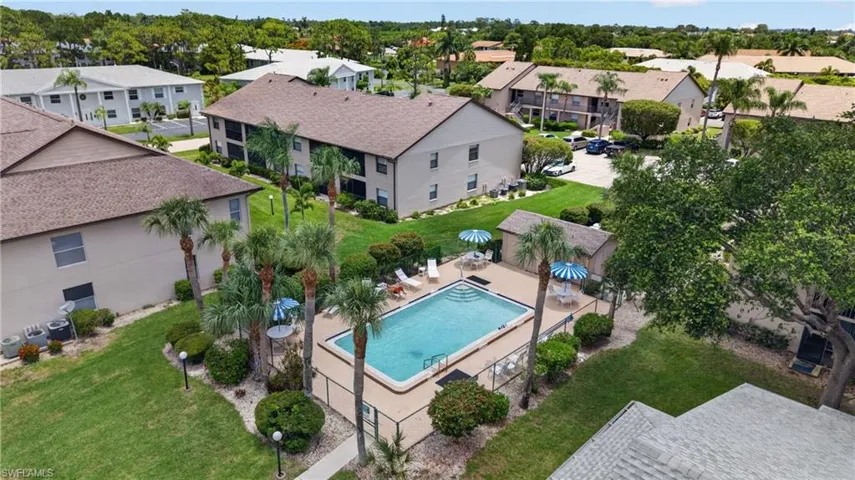 Community swimming pool with surrounding deck and lounge chairs, bordered by mature palm trees and lush landscaping