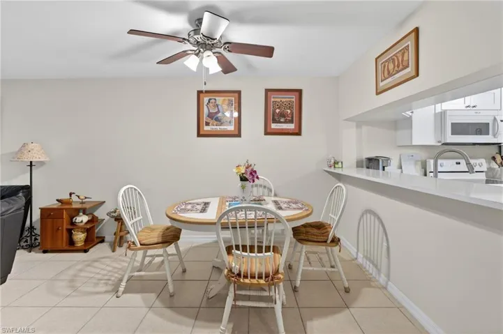 Open concept dining area featuring tile flooring, a ceiling fan, and a kitchen pass-through with a breakfast bar