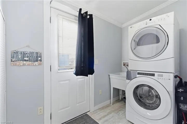 Washroom with stacked washer and clothes dryer, crown molding, and light wood-style flooring