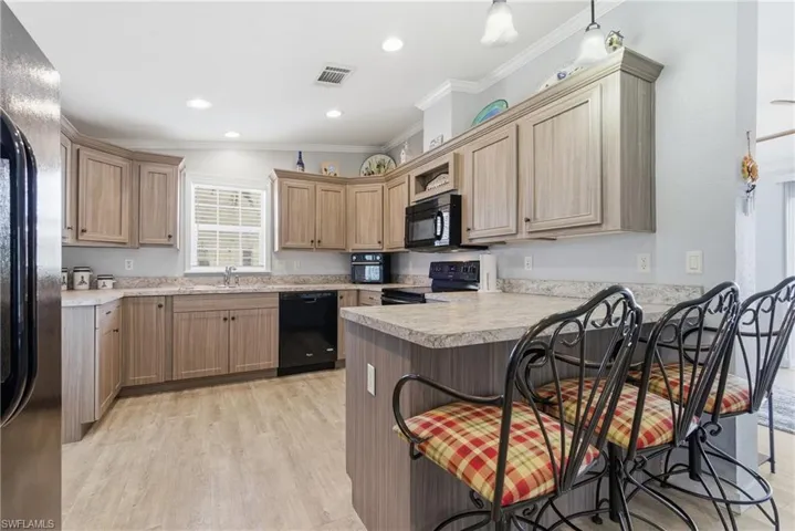 Kitchen featuring a breakfast bar area, ornamental molding, black appliances, a peninsula, and light countertops