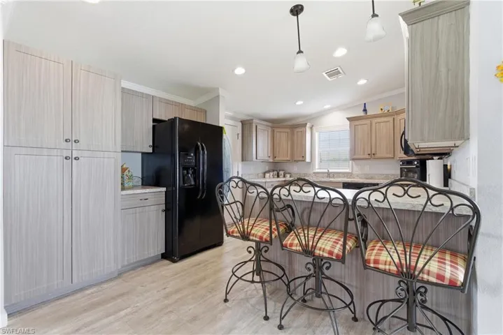 Kitchen featuring a breakfast bar area, ornamental molding, black refrigerator with ice dispenser, a peninsula, and decorative light fixtures
