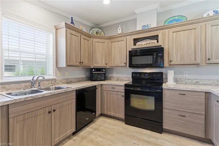 Kitchen with black appliances, light countertops, ornamental molding, light brown cabinetry, and light wood-style flooring