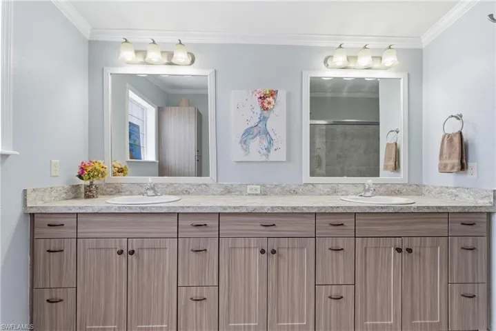 Full bath with double vanity, crown molding, and a shower with shower door