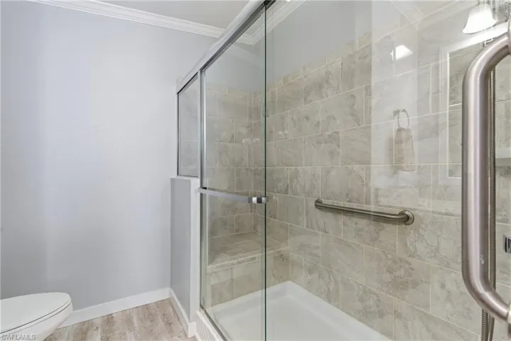 Full bath featuring ornamental molding, a shower stall, and light wood-style flooring