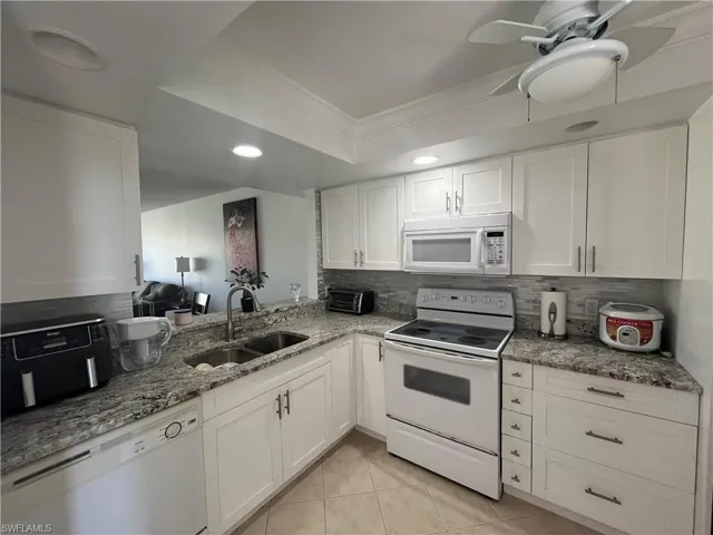 Kitchen featuring light stone countertops, white appliances, white cabinetry, a tray ceiling, and decorative backsplash