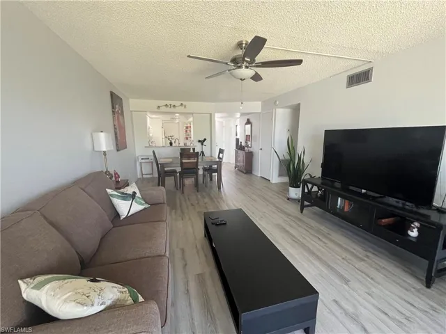 Living area with light wood-type flooring, a textured ceiling, and ceiling fan