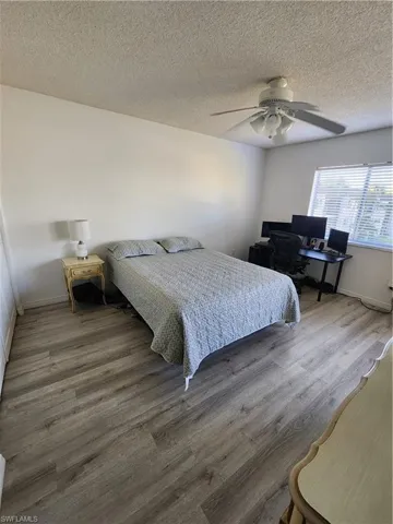 Bedroom with a desk, a ceiling fan, wood finished floors, and a textured ceiling