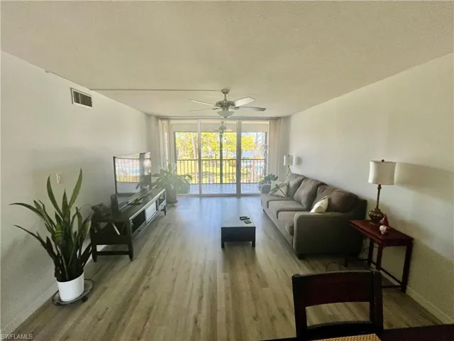 Living area with a wall of windows, a textured ceiling, wood finished floors, and ceiling fan