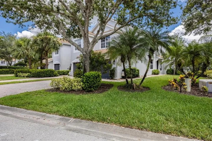 View of property hidden behind natural elements featuring stucco siding, a front lawn, and driveway