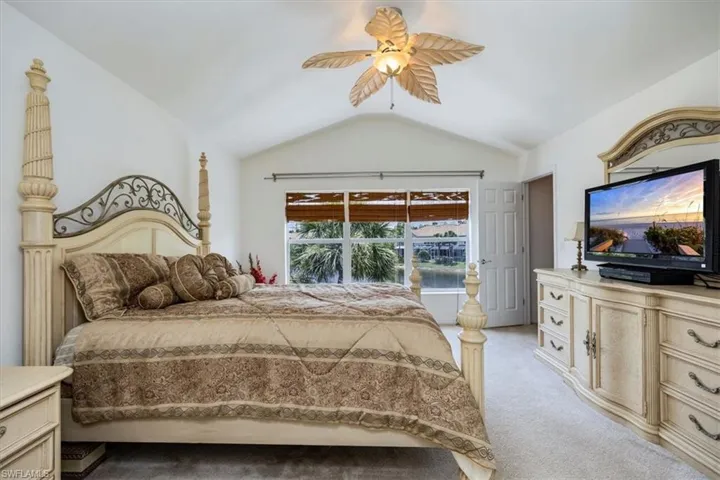Bedroom featuring light colored carpet, vaulted ceiling, and ceiling fan, triple windows with lake view