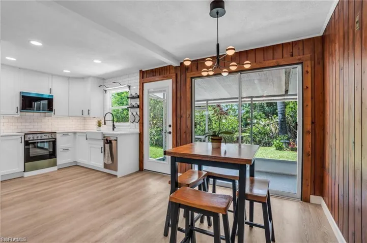 Dining room featuring light wood-style flooring, wood walls, a notable chandelier, and beam ceiling