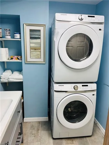Laundry room featuring light wood finished floors, cabinet space, stacked washer and clothes dryer, and baseboards