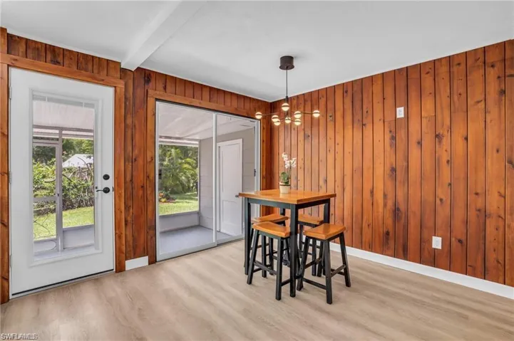 Dining area featuring baseboards, beamed ceiling, wooden walls, and light wood-style flooring