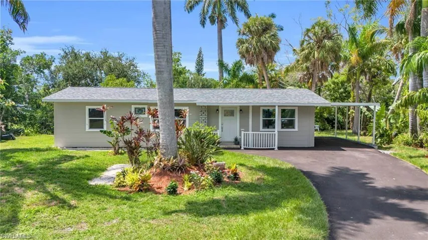 Ranch-style home with aphalt driveway, a front lawn, a shingled roof, a carport, and a porch