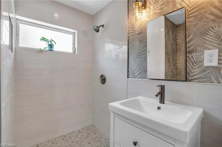 Bathroom featuring vanity, tasteful backsplash, tiled shower, and tile walls