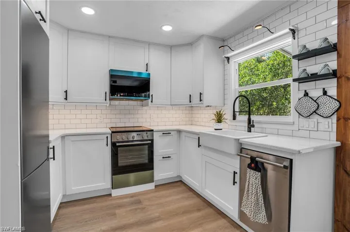 Kitchen featuring a sink, tasteful backsplash, light wood-style flooring, stainless steel appliances, and white cabinets