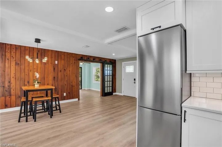 Kitchen with stainless steel refrigerator, visible vents, light wood-style flooring, and white cabinets