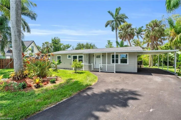 Single story home featuring driveway, an attached carport, fence, a front lawn, and a porch
