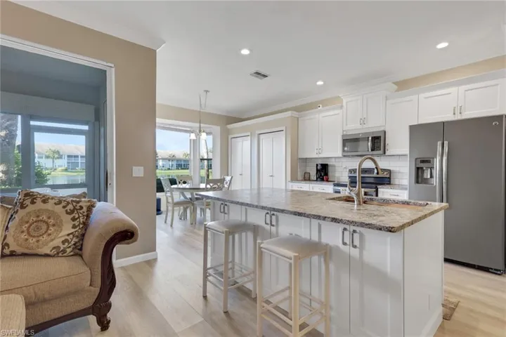 Kitchen with appliances with stainless steel finishes, white cabinetry with soft close cabinets and drawers, tasteful backsplash, light stone counters, and light wood-style floors; granite countertops with protective seal; note additional storage under kitchen island.
