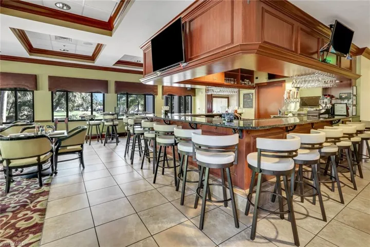 Bar area in community clubhouse featuring dark stone counters, crown molding, and brown cabinetry