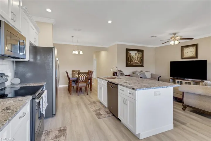 Kitchen featuring stainless steel appliances, white cabinets wit soft close cabinets and drawers, open floor plan, crown molding, and recessed lighting; countertops are granite with a protective seal.