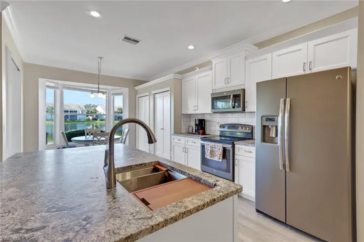 Kitchen featuring stainless steel appliances, white cabinets with soft-close drawers and cabinets, decorative backsplash, granite countertops with protective seal; stainless steel farm sink, and pendant lighting