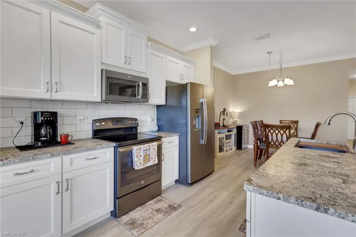 Kitchen featuring stainless steel appliances, backsplash, soft close cabinetry and drawers, ornamental molding, and pendant lighting; countertop is granite with a protective seal.