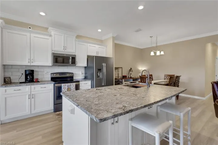 Kitchen featuring granite countertops wit protective seal, soft-close cabinets and drawers, tasteful backsplash, appliances with stainless steel finishes, a kitchen breakfast bar, and crown molding; note additional storage in kitchen island.