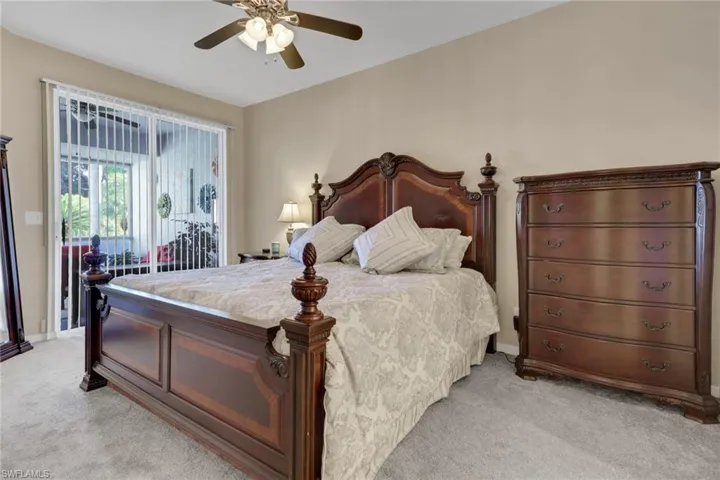 Bedroom featuring light colored carpet, ceiling fan, and access to exterior screened-in lanai at front of the villa.