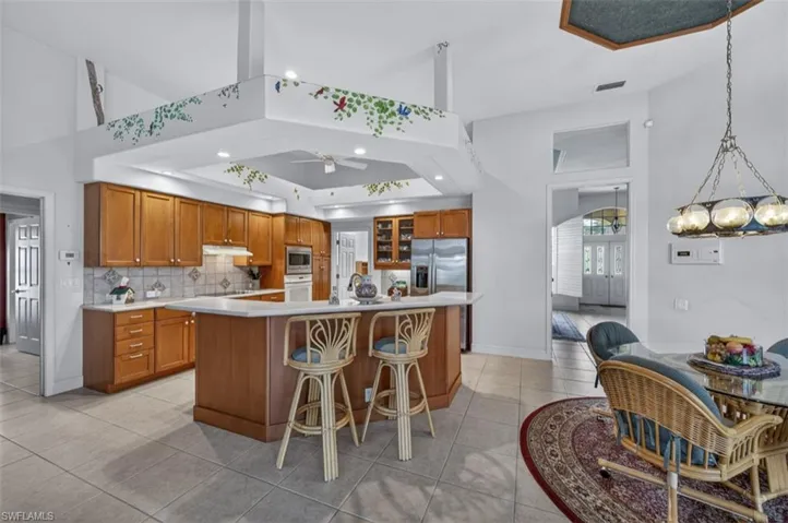 Kitchen with a breakfast bar, wood finish cabinets, light countertops, glass insert cabinets, and a kitchen island with sink