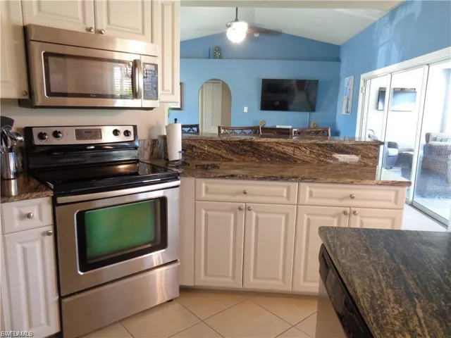 Kitchen featuring stainless steel appliances, dark stone counters, light tile patterned floors, arched walkways, and vaulted ceiling