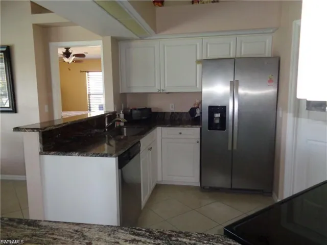 Kitchen featuring stainless steel appliances, dark stone countertops, a peninsula, white cabinetry, and light tile patterned flooring