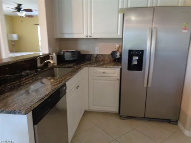 Kitchen with stainless steel appliances, dark stone countertops, white cabinets, and light tile patterned floors