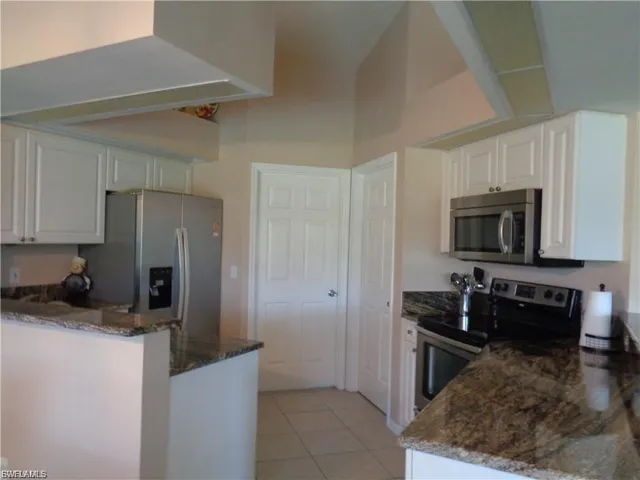 Kitchen featuring a peninsula, dark stone counters, stainless steel appliances, and white cabinetry