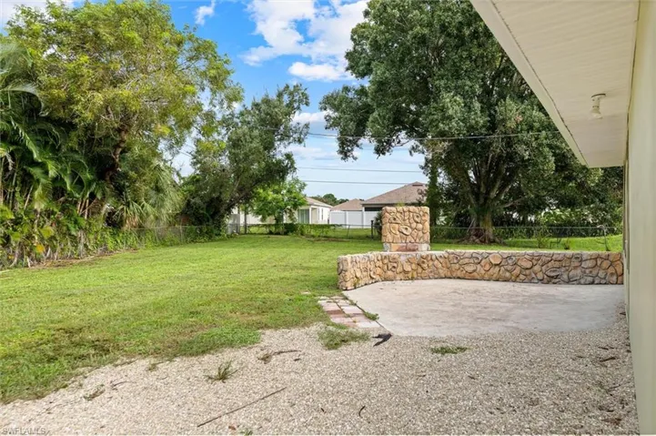 Expansive backyard featuring a stone-clad patio with a built-in stone fireplace, a large grassed area, and mature trees