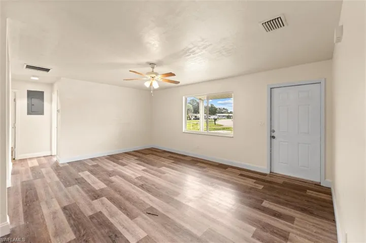 Expansive room featuring wood-finish flooring, a ceiling fan, and a paneled entry door