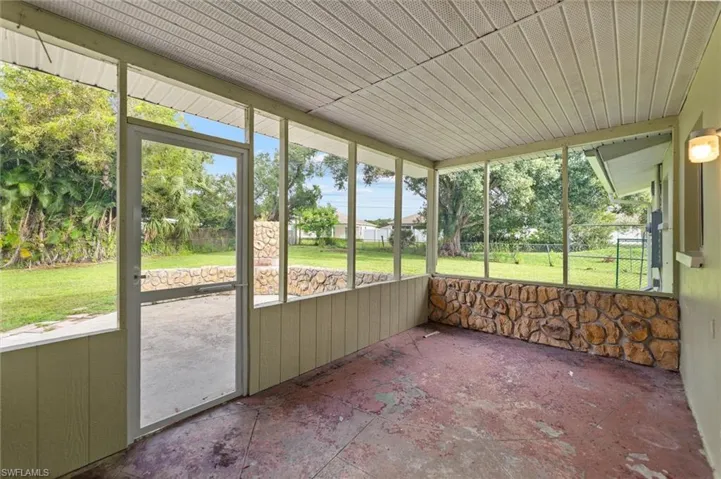 Screened patio with a textured stone half-wall, a ceiling light fixture, and a screened door leading to the backyard