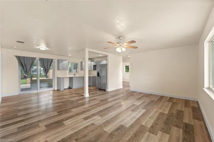 Open-concept living area with wood-finish flooring, a ceiling fan, and abundant natural light from multiple windows and sliding glass doors