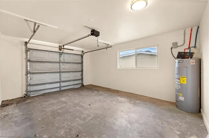 Spacious garage featuring an automatic overhead door with integrated opener, concrete flooring, natural light from a transom window, and a tankless water heater with visible plumbing connections