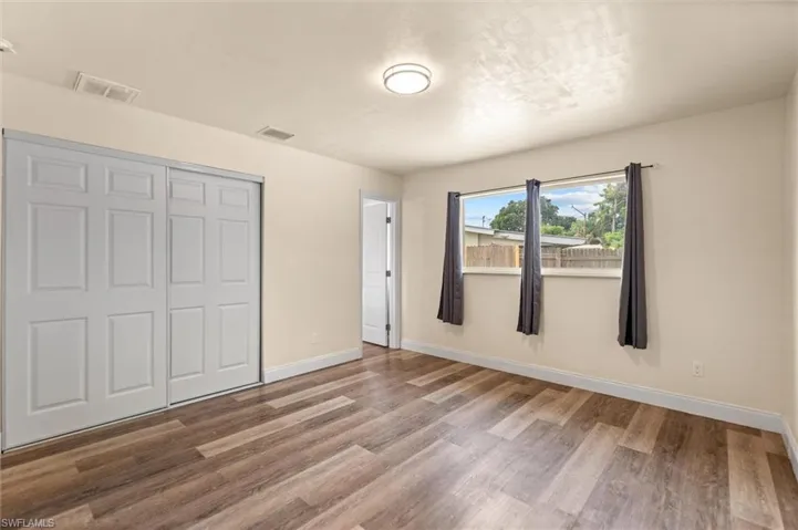Wood-finish flooring, sliding closet doors, ceiling-mounted light fixture, and three window openings