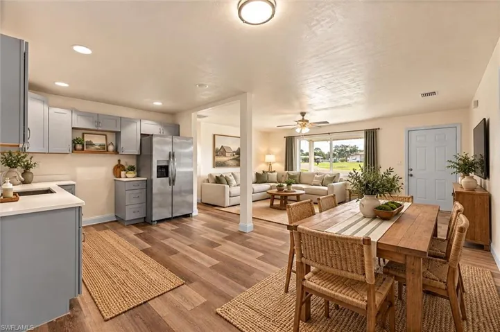 Virtually Staged Open-concept living area with wood-finish flooring, a contemporary kitchen featuring light-toned cabinetry, and a stainless steel refrigerator
