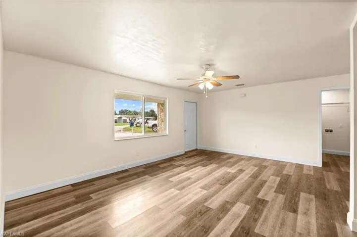 Expansive room featuring wood-finish flooring, a ceiling fan with integrated lighting, and a large window