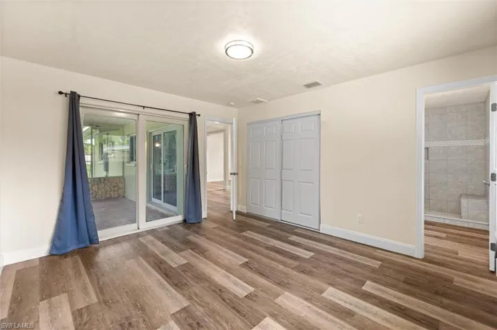 Wood-finish flooring, sliding glass doors to outdoor space, built-in closet with bifold doors, and an attached shower with tiled walls and built-in bench