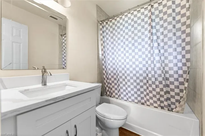 White vanity with an integrated sink and brushed nickel faucet, a framed mirror, and a white bathtub with tiled surround
