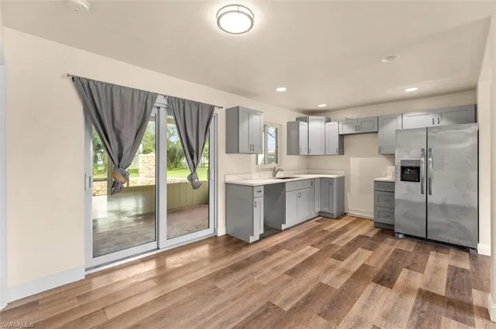 Wood-finish flooring, light gray cabinetry, stainless steel refrigerator, white countertops, and sliding glass doors