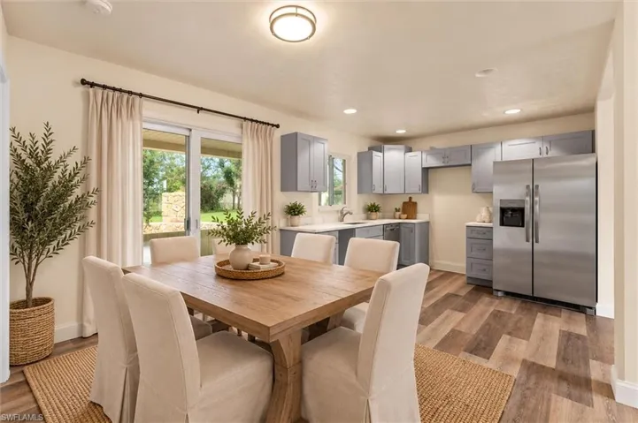 Virtually Staged Open-concept dining area with wood-finish flooring, sliding glass doors, contemporary ceiling light fixture, light gray cabinetry, and stainless steel refrigerator