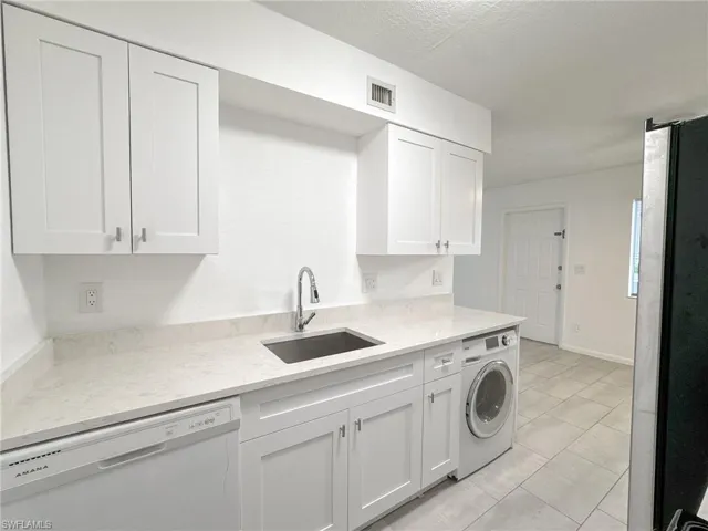 Kitchen with dishwasher, white cabinetry, freestanding refrigerator, washer / clothes dryer, and light tile patterned flooring