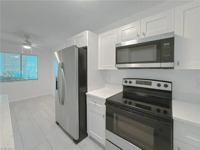 Kitchen with appliances with stainless steel finishes, white cabinetry, a ceiling fan, light stone counters, and light tile patterned flooring